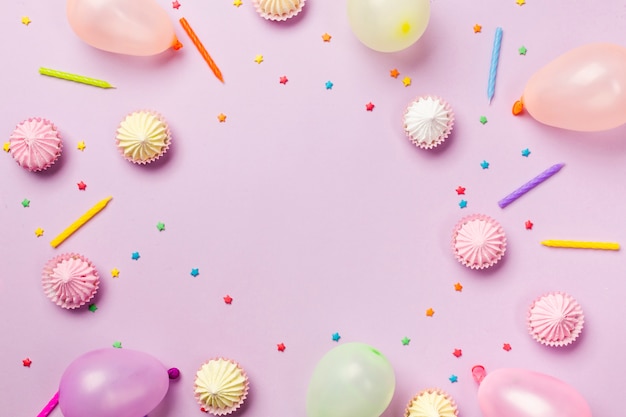 An elevated view of sprinkles; candles; balloons; aalaw on pink background