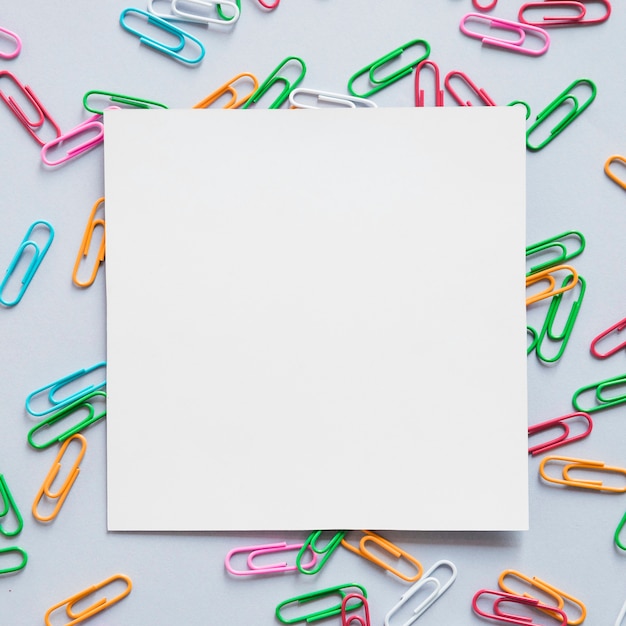 Elevated view of square shaped cardboard paper and many paper clips on grey background