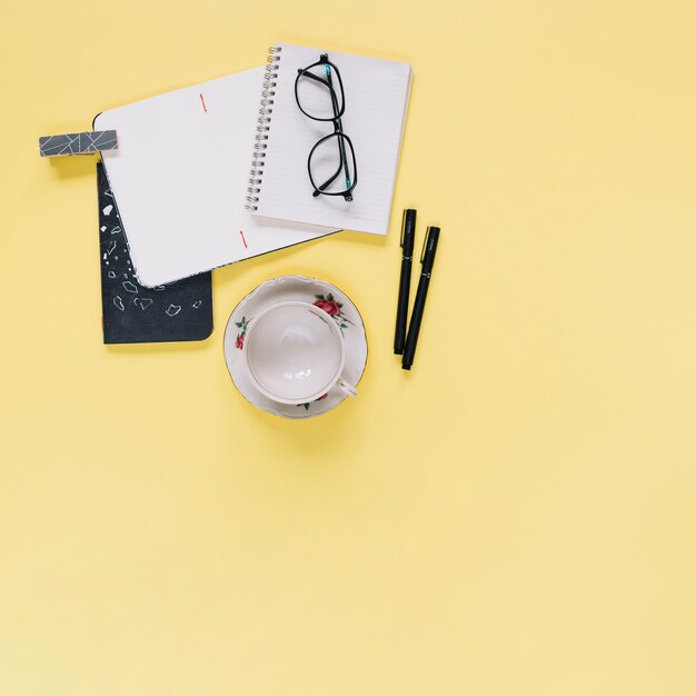 Elevated view of stationeries and empty cup on yellow backdrop