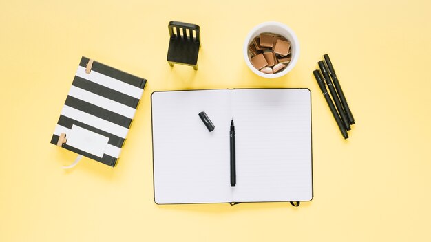 Elevated view of stationeries and glass of chocolates on yellow background