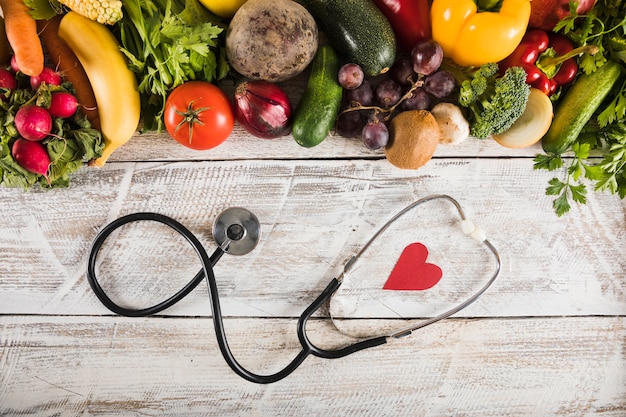 Elevated view of stethoscope with heart shape near fresh vegetables on wooden desk