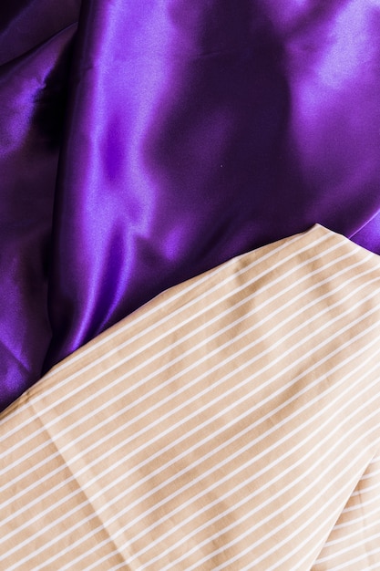 Повышенный вид текстильной ткани с прямыми линиями на шелковистой фиолетовой драпе