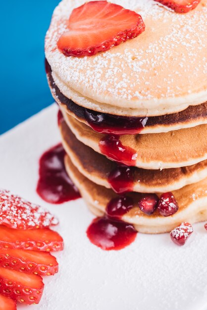 An elevated view of strawberry slice on stacked of pancake with berry sauce