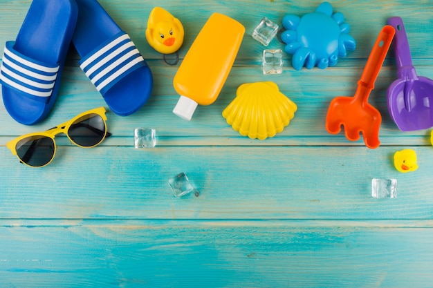 An elevated view of sunglasses; ice cubes; flip-flop; rubber duck; toys on turquoise wooden desk