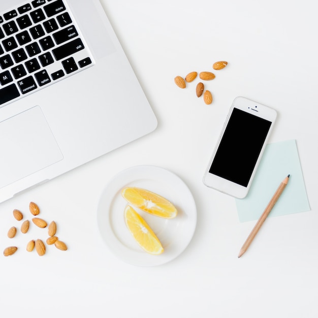 Elevated view of sweet lime; pencil; cellphone and laptop on white backdrop