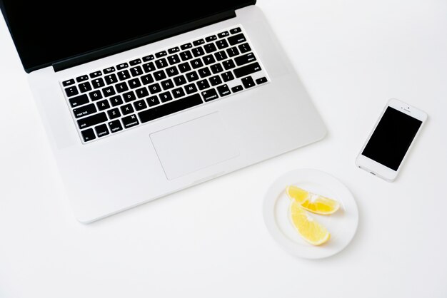 Elevated view of sweet lime; smartphone and laptop on white background