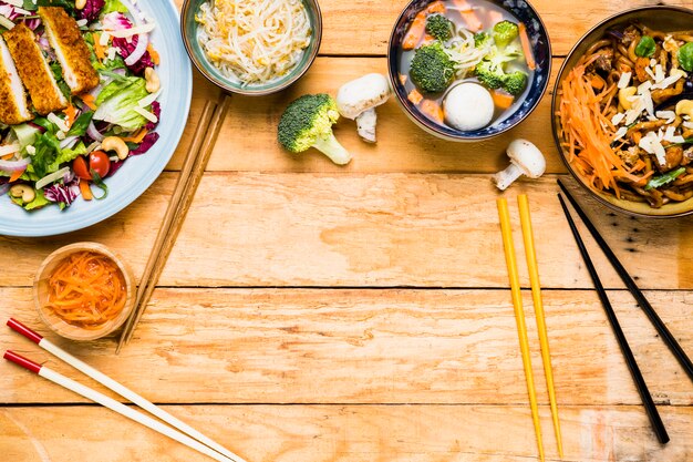 An elevated view of thai salad; sprouts; fish ball soup and noodles with different type of chopsticks on wooden table