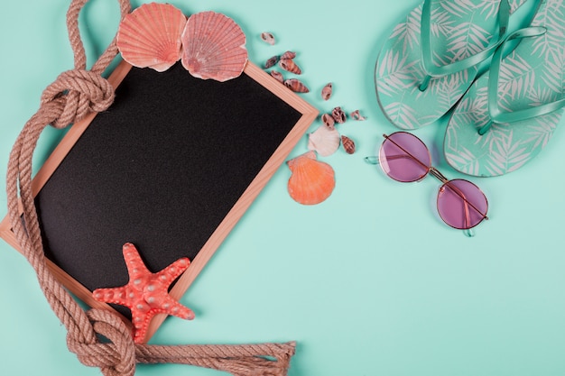 Free photo an elevated view of tied rope with seashells; sunglasses and pair of flippers on mint backdrop