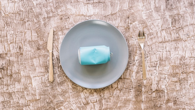 Elevated view of tin can on plate between kitchen knife and fork