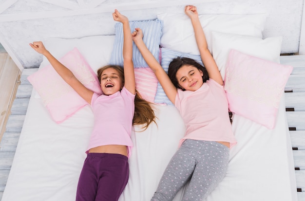 Free photo an elevated view of two girls stretching their arms while waking up on bed