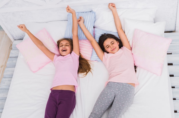 Поднятый вид двух девушек, протягивающих руки, просыпаясь на кровати