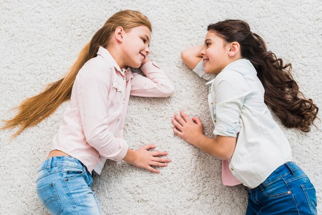 An elevated view of two smiling girls lying on carpet looking at each other