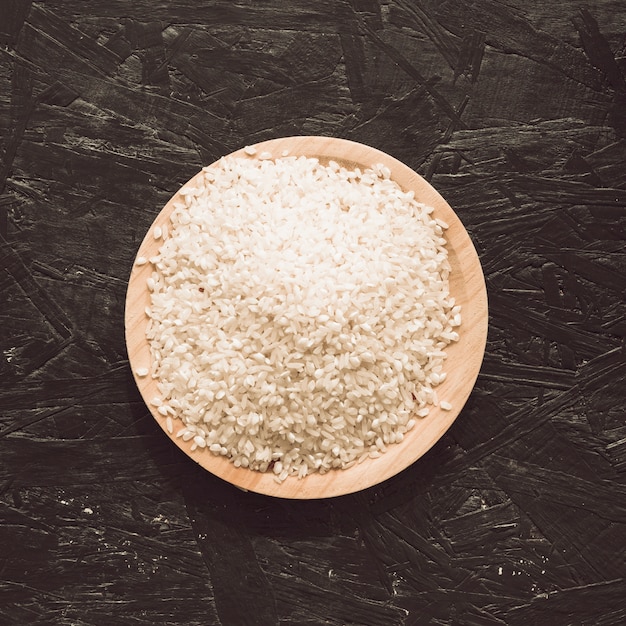 Elevated view of uncooked rice grains in bowl on rough gray background