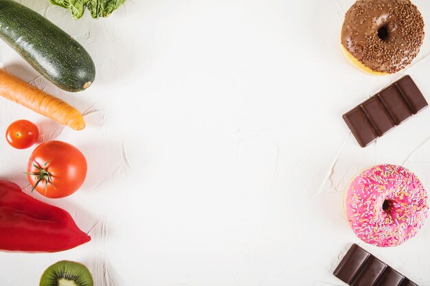 Elevated view of unhealthy food against healthy vegetables on white background