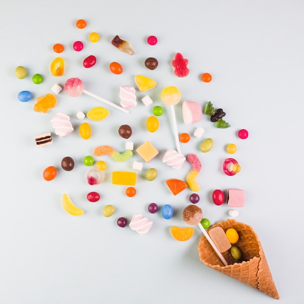 Elevated view of various candies with ice cream waffle cone on white background