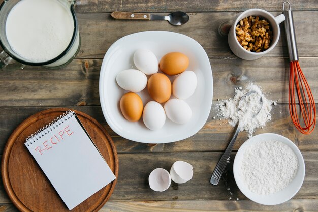 Foto gratuita vista elevata di vari ingredienti con il blocco note a spirale che mostra la parola di ricetta