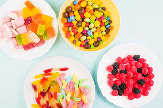 Elevated view of various sweet candies on plate over colored background