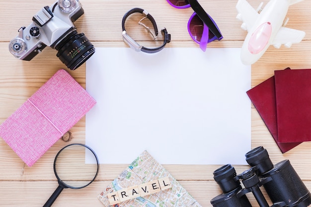 Elevated view of various traveling equipments and blank white paper on wooden backdrop