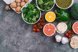 Free photo an elevated view of vegetables; eggs; citrus fruit and puffed rice cake on gray concrete backdrop