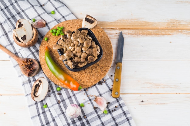 Elevated view of vegetables; spices and kitchen utensil on tablecloth over wooden table