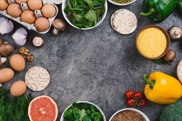 An elevated view of vegetables; walnuts; fruits and puffed rice cake on gray concrete backdrop