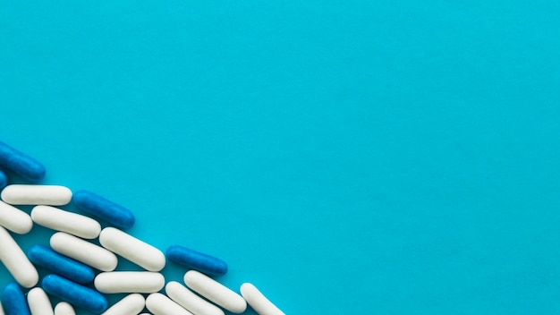 Elevated view of white and blue candy capsules at the corner of cyan backdrop