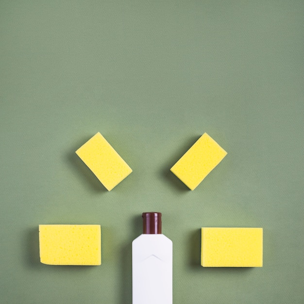 Elevated view of white bottle and yellow sponge on green background