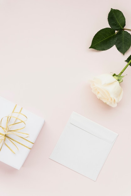 Elevated view of white flower; gift and envelope on colored backdrop