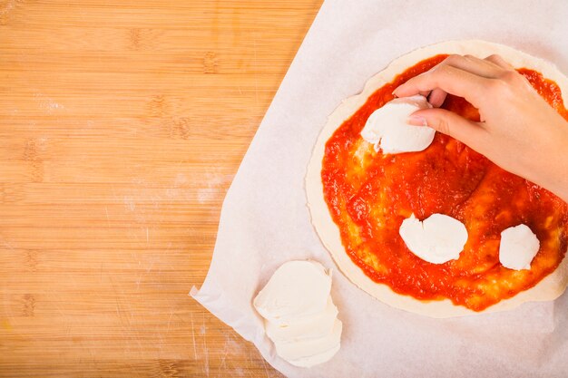 Elevated view of a woman's hand putting cheese on dough