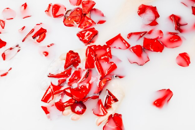 Elevated view of woman's hand and red flower petals in spa bath with milk