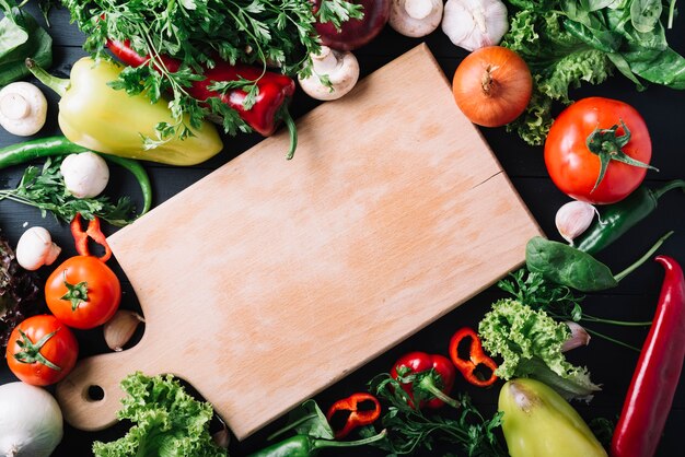 Elevated view of wooden chopping board surrounded with fresh vegetables
