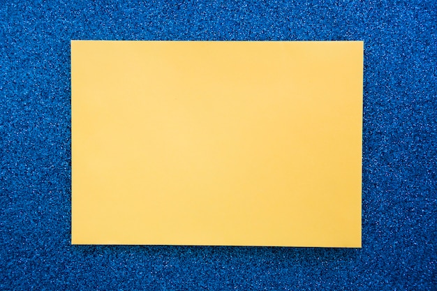 Elevated view of yellow cardboard paper on blue backdrop