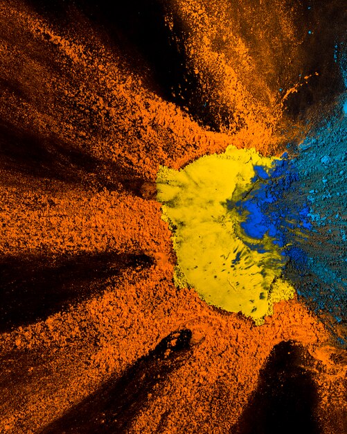 Elevated view of yellow,orange and blue holi powder design on black backdrop