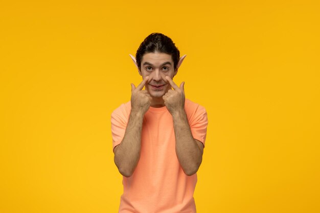 Elf guy happy handsome pretty guy in orange tshirt stretching eyes with elf ears