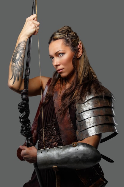 灰色の背景に分離された弓を持つ鎧のエルフの女性。