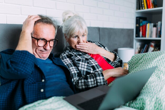 Embarrassed elderly couple in bed with laptop