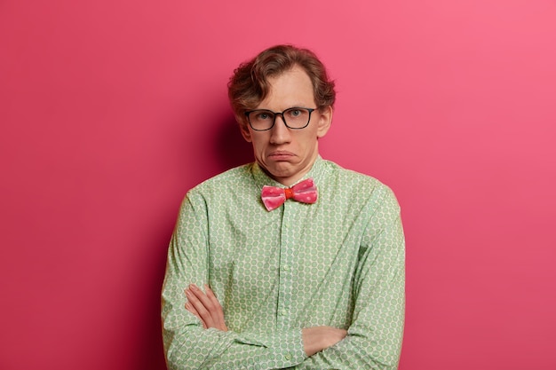 Free photo embarrassed hesitant man looks confusingly , crosses hands, has unaware face expression, thinks about changing job position, dressed formally, has serious look, isolated on pink wall