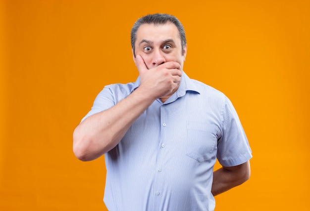 Смущенный мужчина средних лет в синей рубашке в вертикальную полоску прикрывает рот рукой