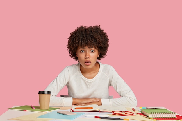 Free photo embarrassed student girl posing at the desk against the pink wall