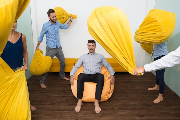 Free photo embarrassed young man among pillow fighting people