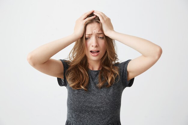 Embarrassed young pretty girl holding her head looking down .