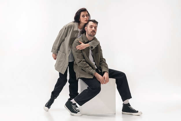 Embracing. Trendy fashionable couple isolated on white studio background. Caucasian woman and man posing in basic minimal stylish clothes. Concept of relations, fashion, beauty, love. Copyspace.