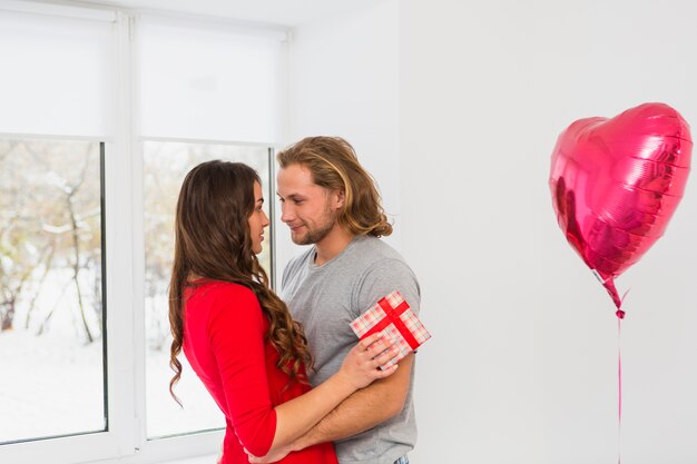 Embracing young couple standing near the pink inflatable heart shape balloon