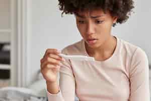 Free photo embrarrassed woman with afro hairstyle faces serious problem, dissatisfied with pregnancy test