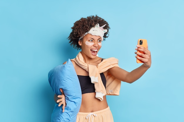 Emotional African American woman exclaims angrily while makes selfie on smartphone prepares for bedtime