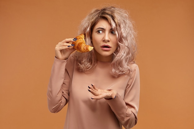 Emotional attractive young woman with messy hairstyle having confused perplexed facial expression, opening mouth