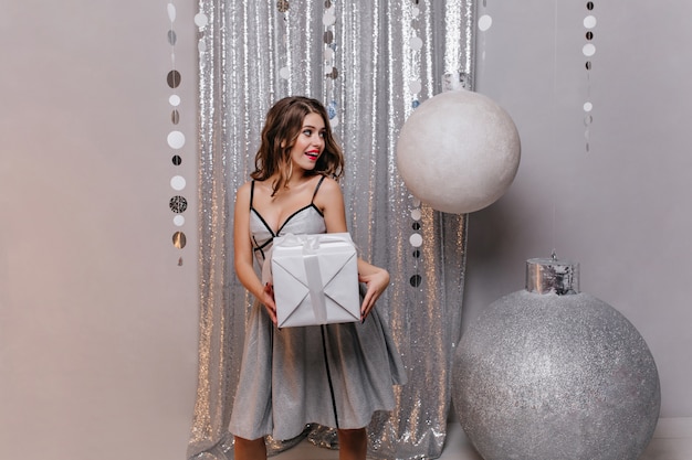 Emotional beautiful brunette in shining dress wants to follow surprise to her friend and give New Year's gift.