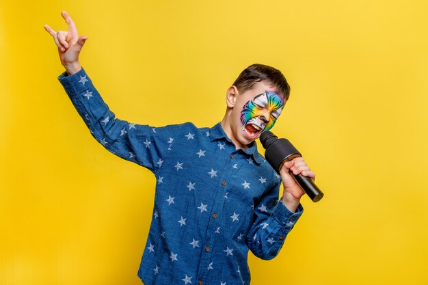 Emotional boy holding karaoke microphone and sing while stay isolated on yellow wall