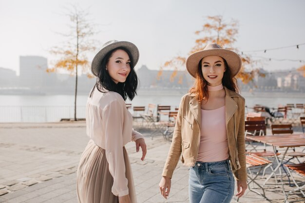 Emotional brunette woman looking over shoulder while joking with her friend