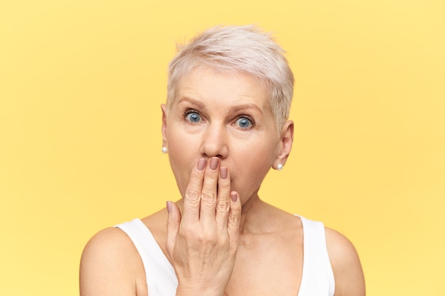 Free photo emotional bug eyed mature female with short hair expressing full disbelief, covering mouth with hand, overhearing intriguing secret, unexpected news or gossip.